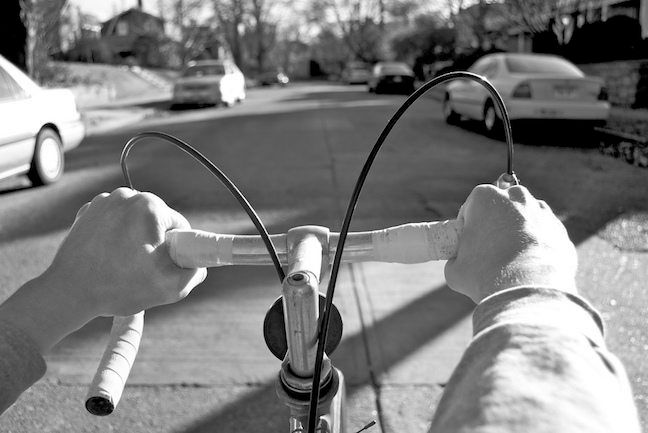 A man’s hands are on the handlebars of a bicycle. as we look down the street from his point-of-view