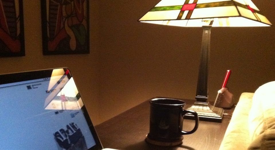 a color photo of a mac laptop, a cup of coffee bathed in light