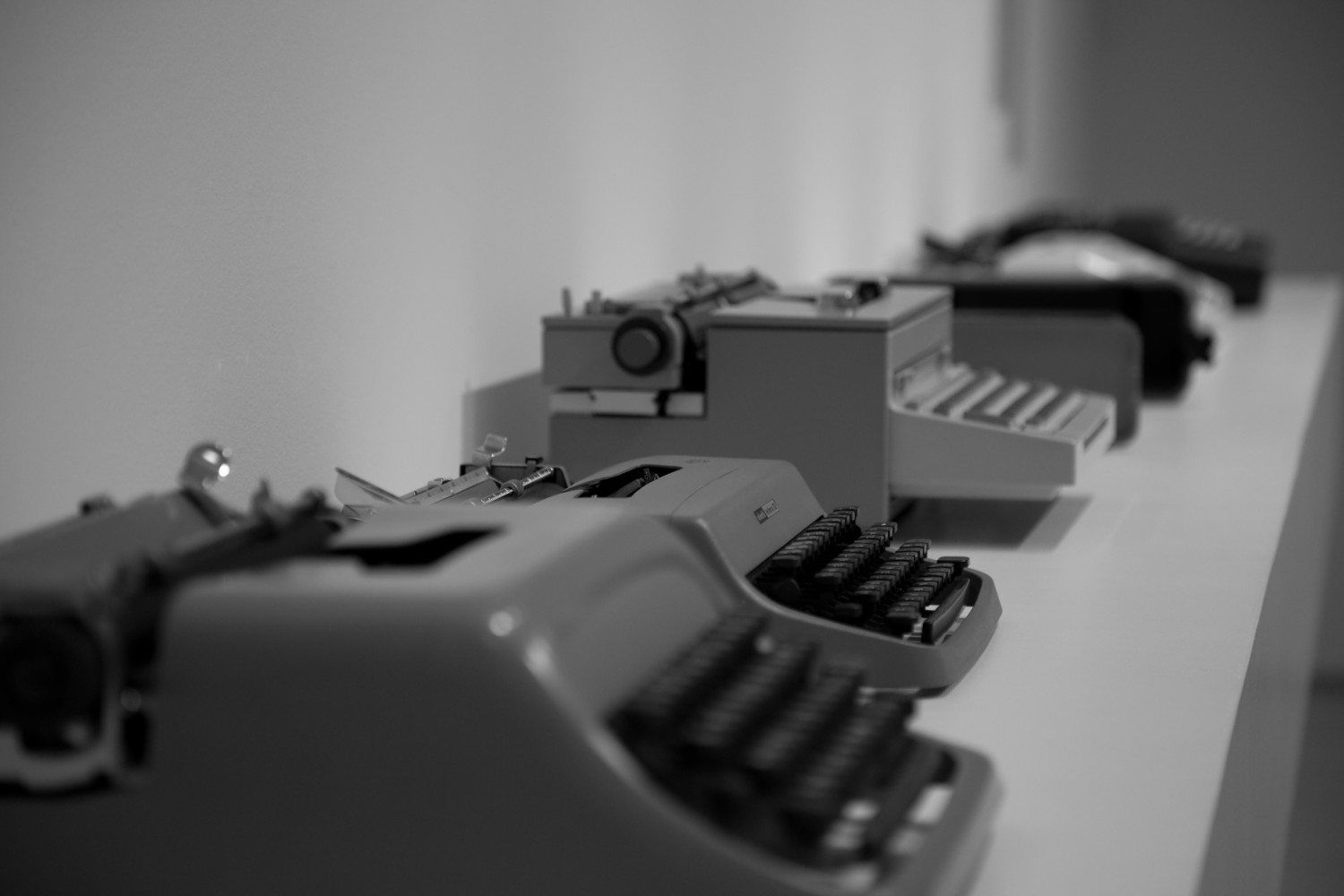 Several typewriters in a row on a long table.