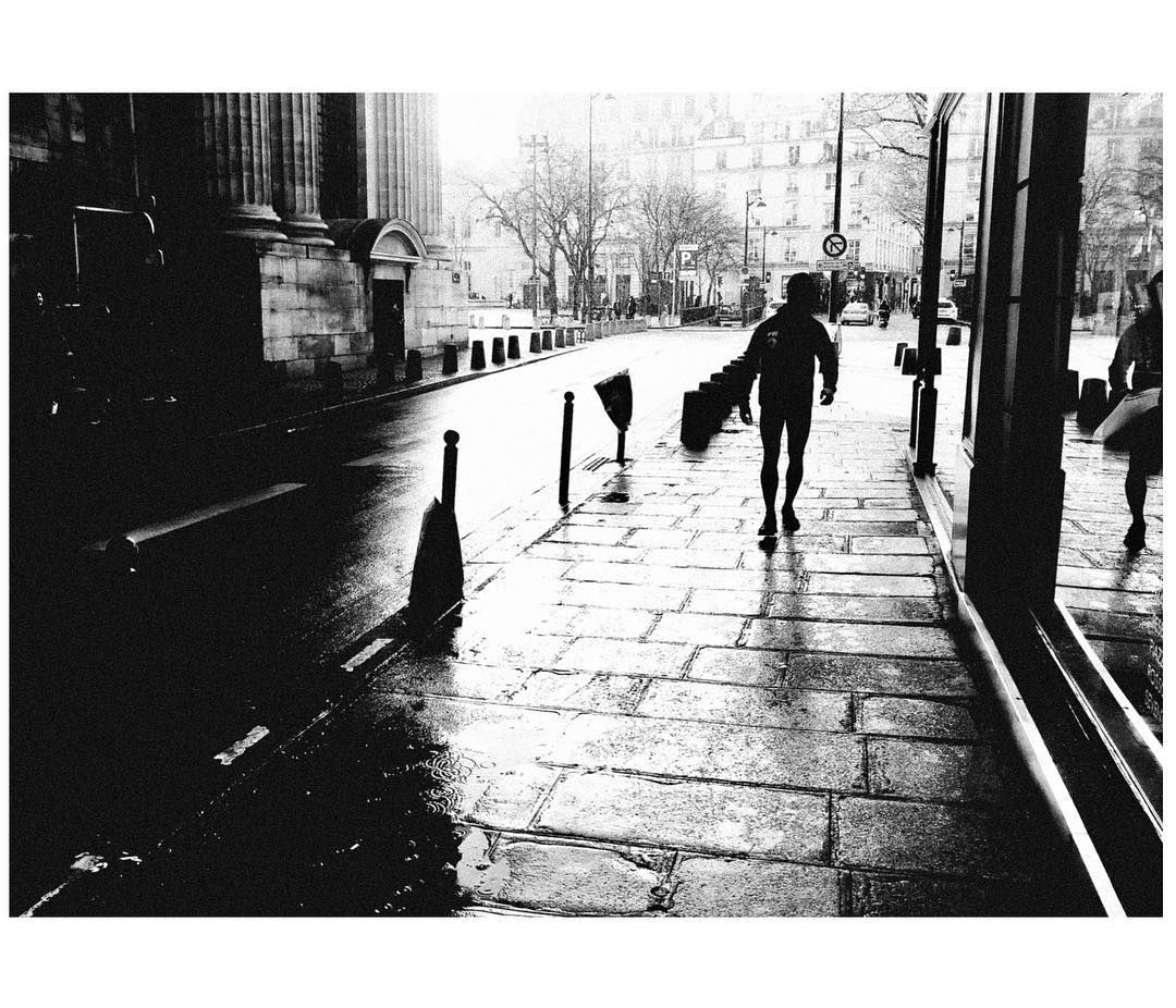 A man carries a long package on a rainy day by St. Sulpice in Paris. Shot with a Ricoh GR2 in black and white by Jay Sennett
