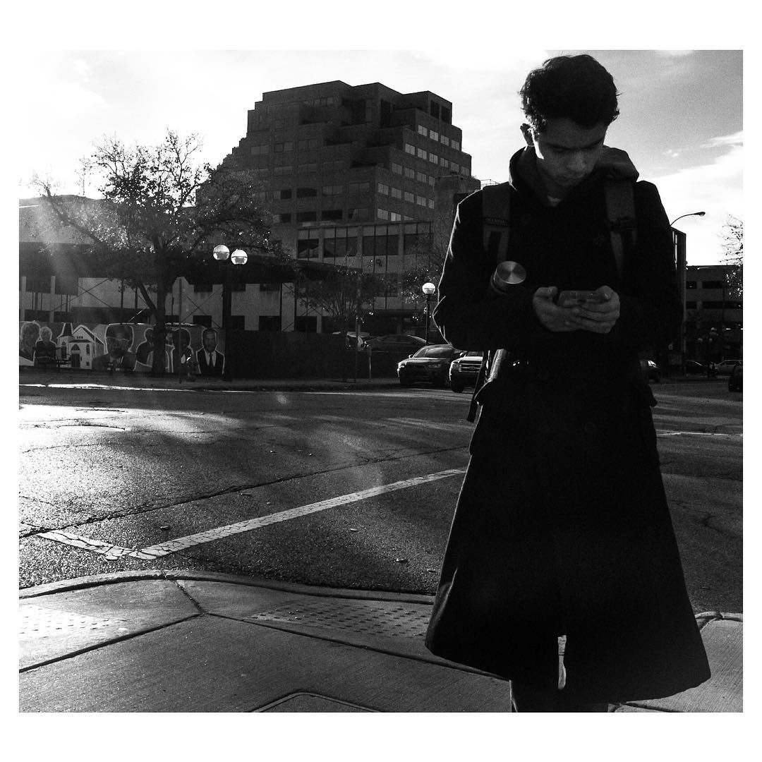 A young man reads his phone on a street corner. Shot by Jay Sennett